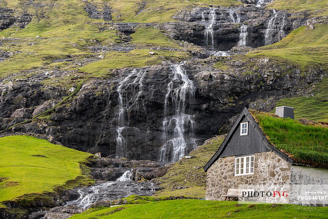 A turf covered house in front of a waterfall in Saksun village on Streymoy island, Faeroe islands, Denmark, Europe